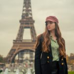 Mulher usando boina e casaco elegante posa diante da Torre Eiffel, em Paris.