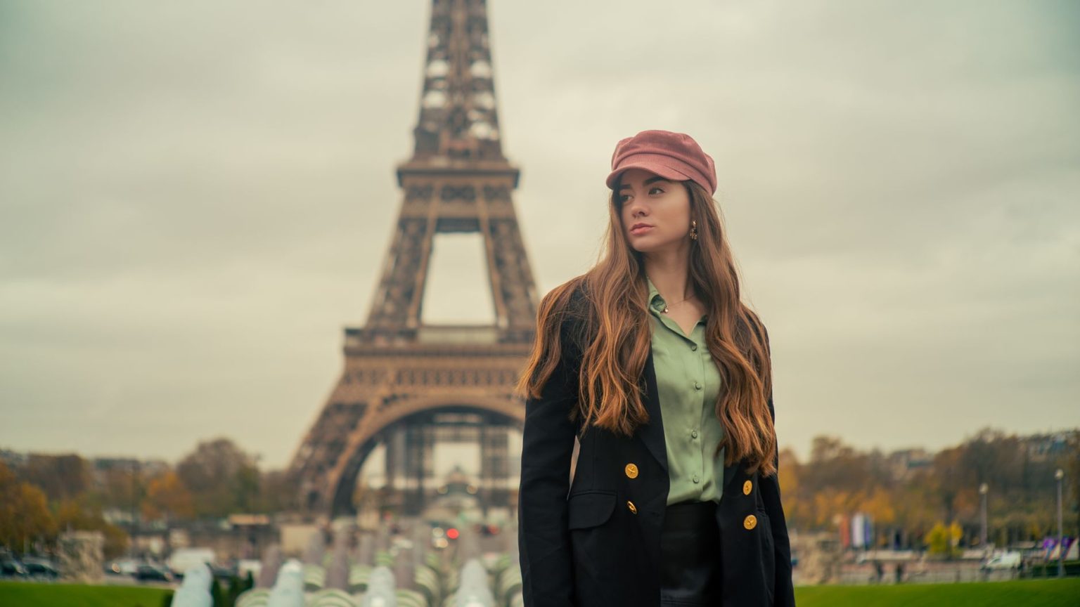 Mulher usando boina e casaco elegante posa diante da Torre Eiffel, em Paris.