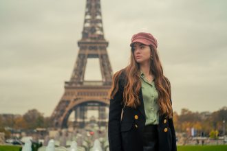 Mulher usando boina e casaco elegante posa diante da Torre Eiffel, em Paris.