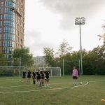 Jogadoras de futebol treinam em grupo em um campo ao ar livre, acompanhadas por uma treinadora.