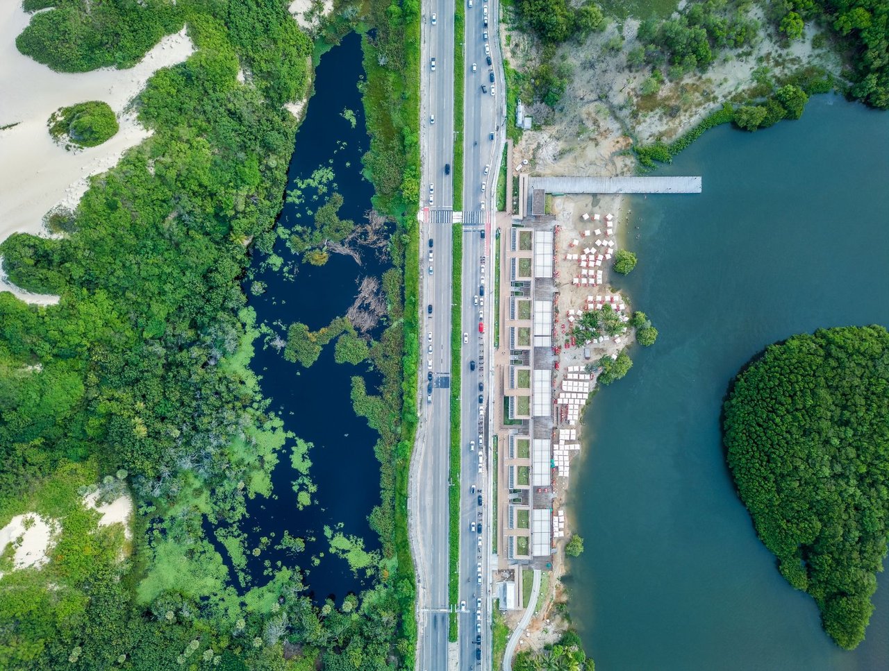 Vista aérea de área urbana junto ao litoral, com estrada, vegetação e faixa costeira em Fortaleza.