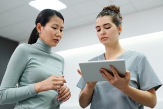 Duas mulheres conversam durante uma consulta de saúde, utilizando um tablet em um ambiente interno.