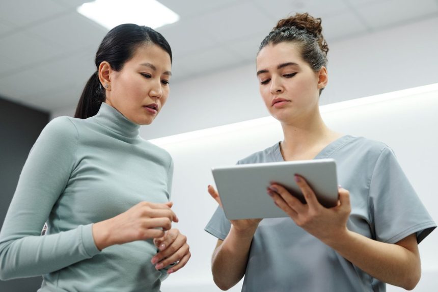 Duas mulheres conversam durante uma consulta de saúde, utilizando um tablet em um ambiente interno.