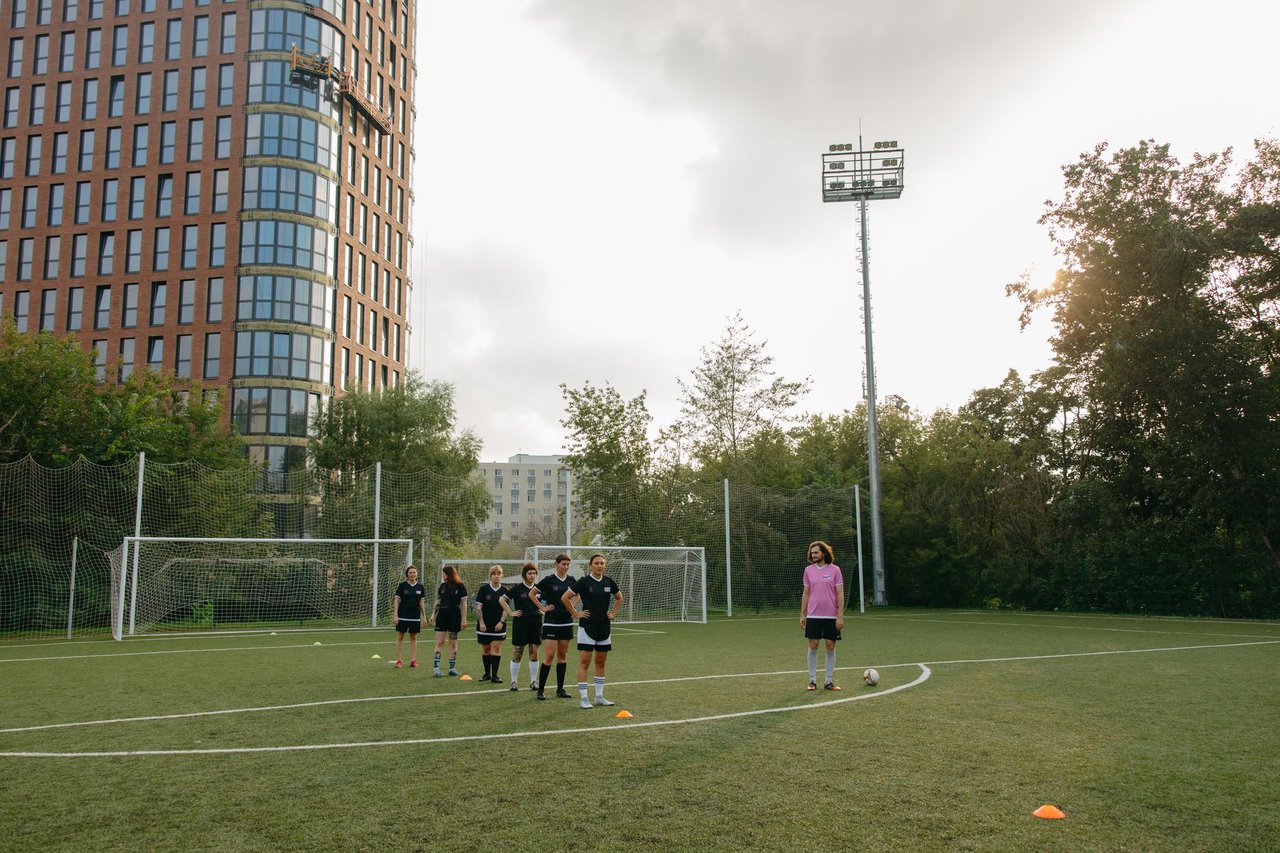 Jogadoras de futebol treinam em grupo em um campo ao ar livre, acompanhadas por uma treinadora.