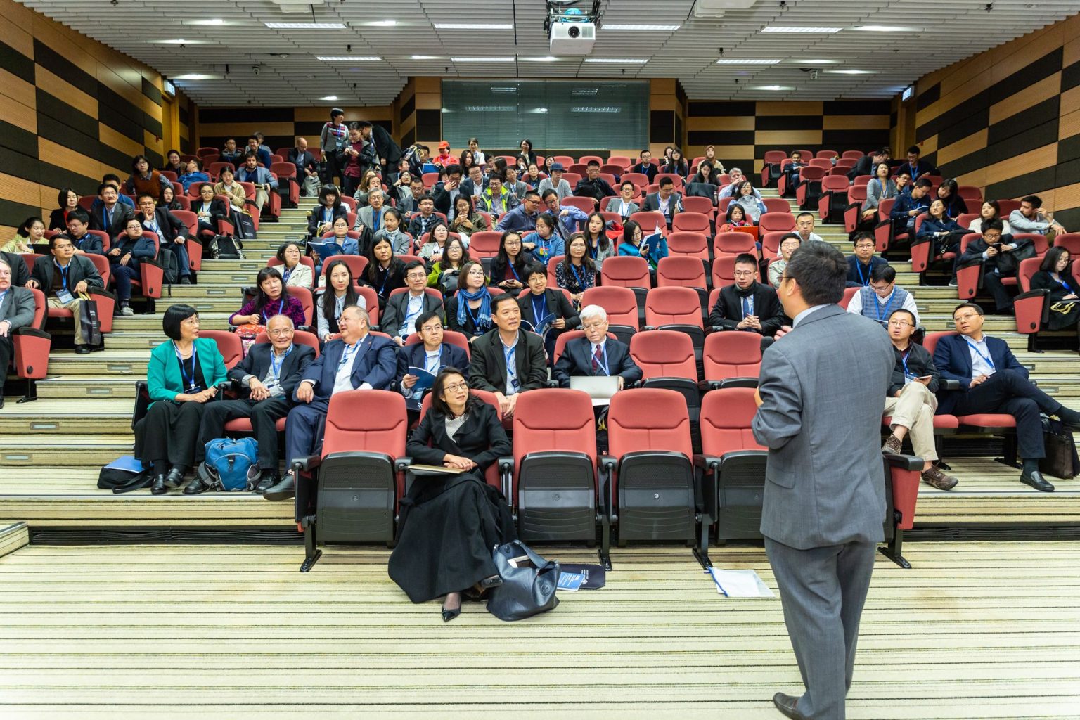 Participantes acompanham uma apresentação em um auditório durante uma conferência.