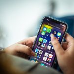 Mulher segurando um smartphone com vários aplicativos exibidos na tela.