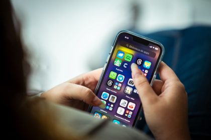 Mulher segurando um smartphone com vários aplicativos exibidos na tela.