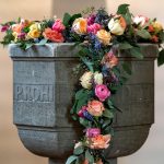 Fonte batismal decorada com flores no interior de uma capela cristã.