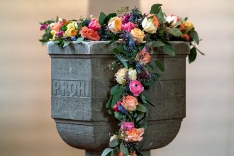 Fonte batismal decorada com flores no interior de uma capela cristã.