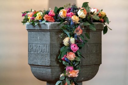 Fonte batismal decorada com flores no interior de uma capela cristã.